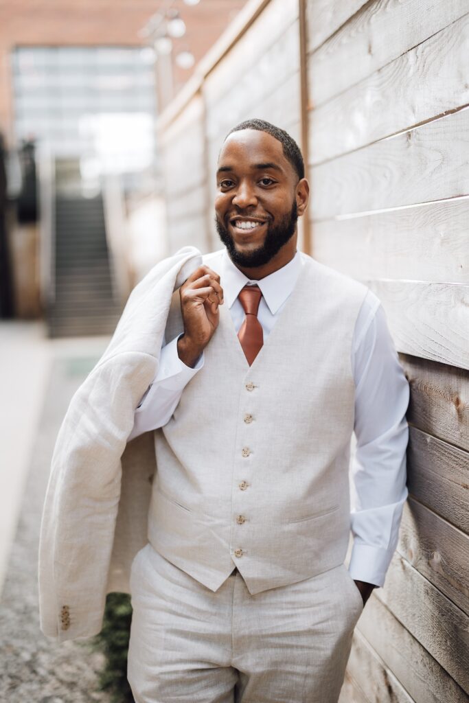 groom leaning against a wall with his jacket over his shoulder at their Ozari Nashville wedding