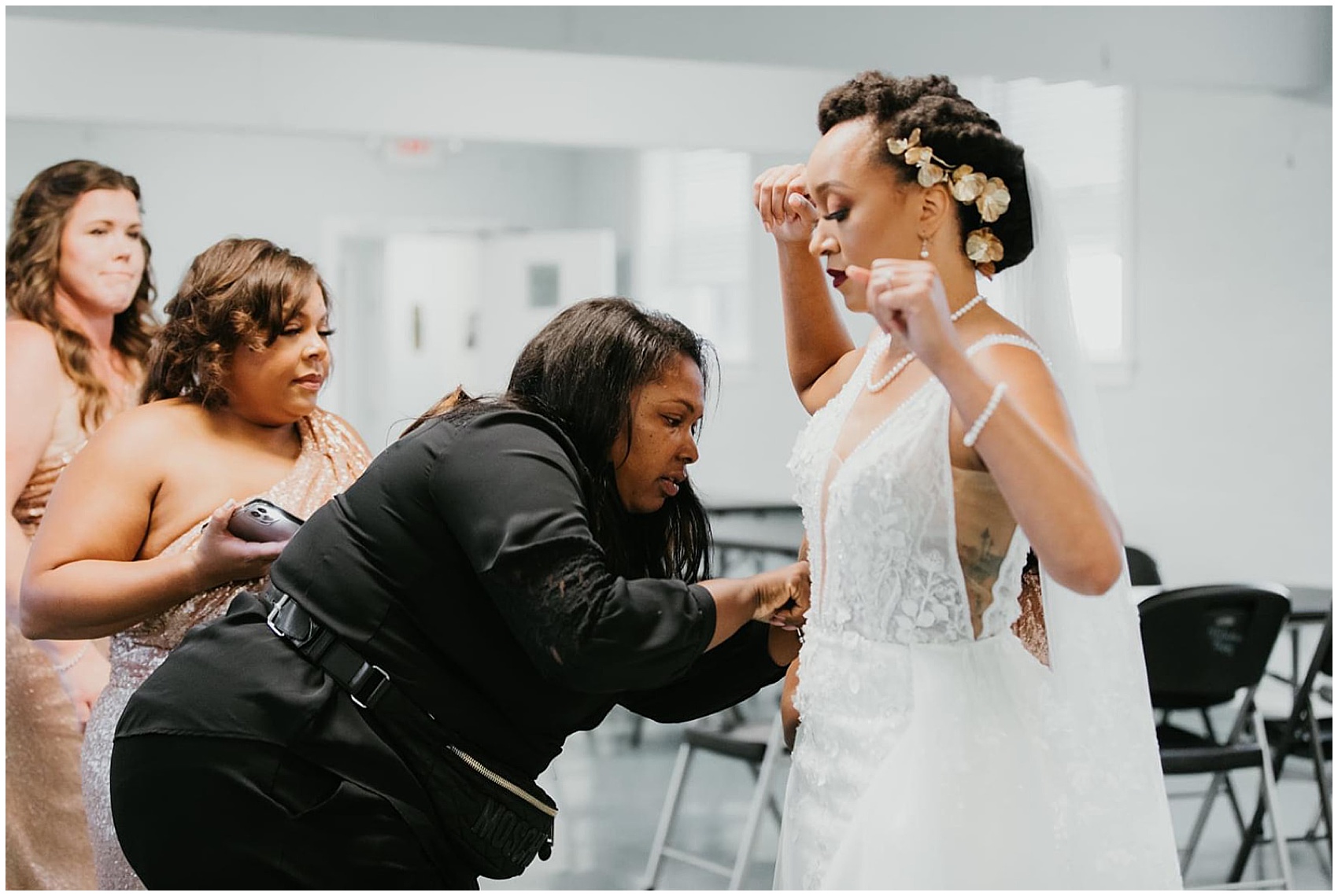Wedding coordinator helps a bride get into her dress with bridesmaids PLS Coordinate