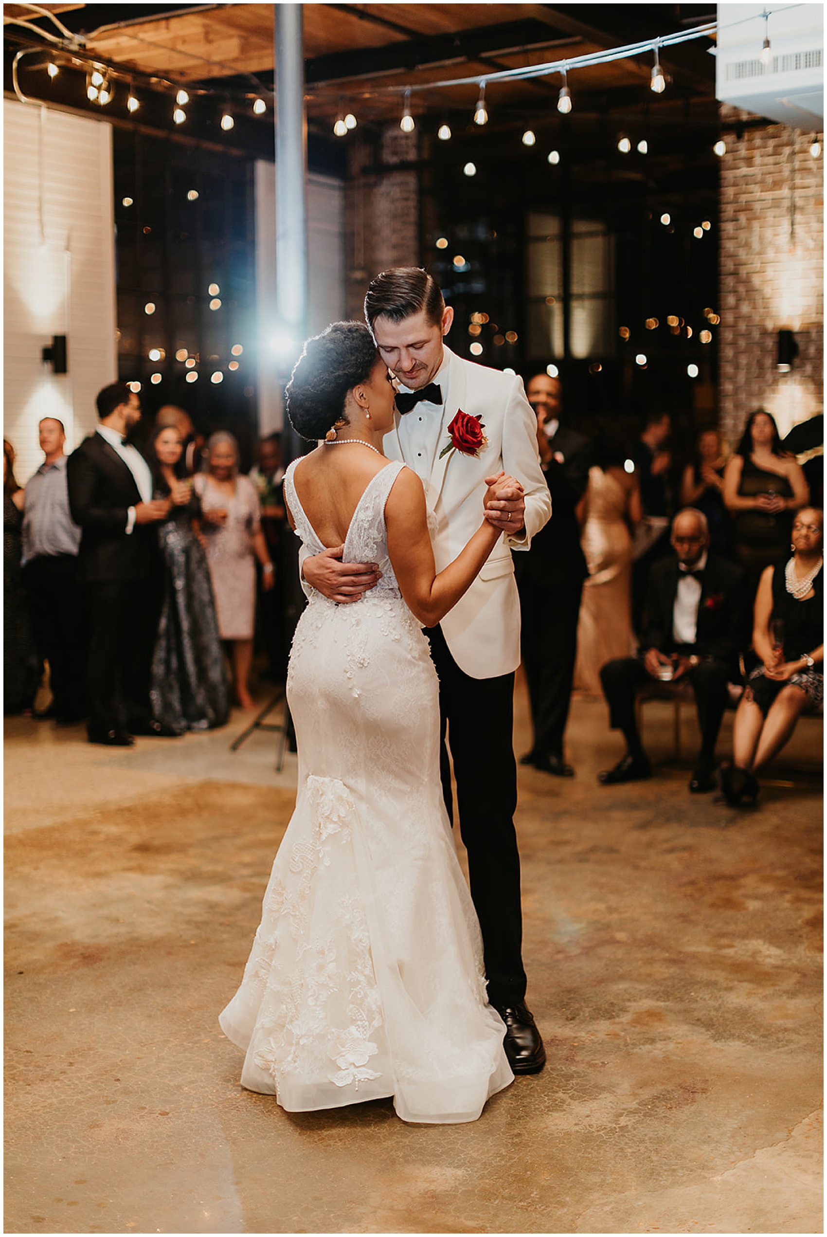 Newlyweds dance alone on the dance floor wearing a white jacket with red rose boutonniere