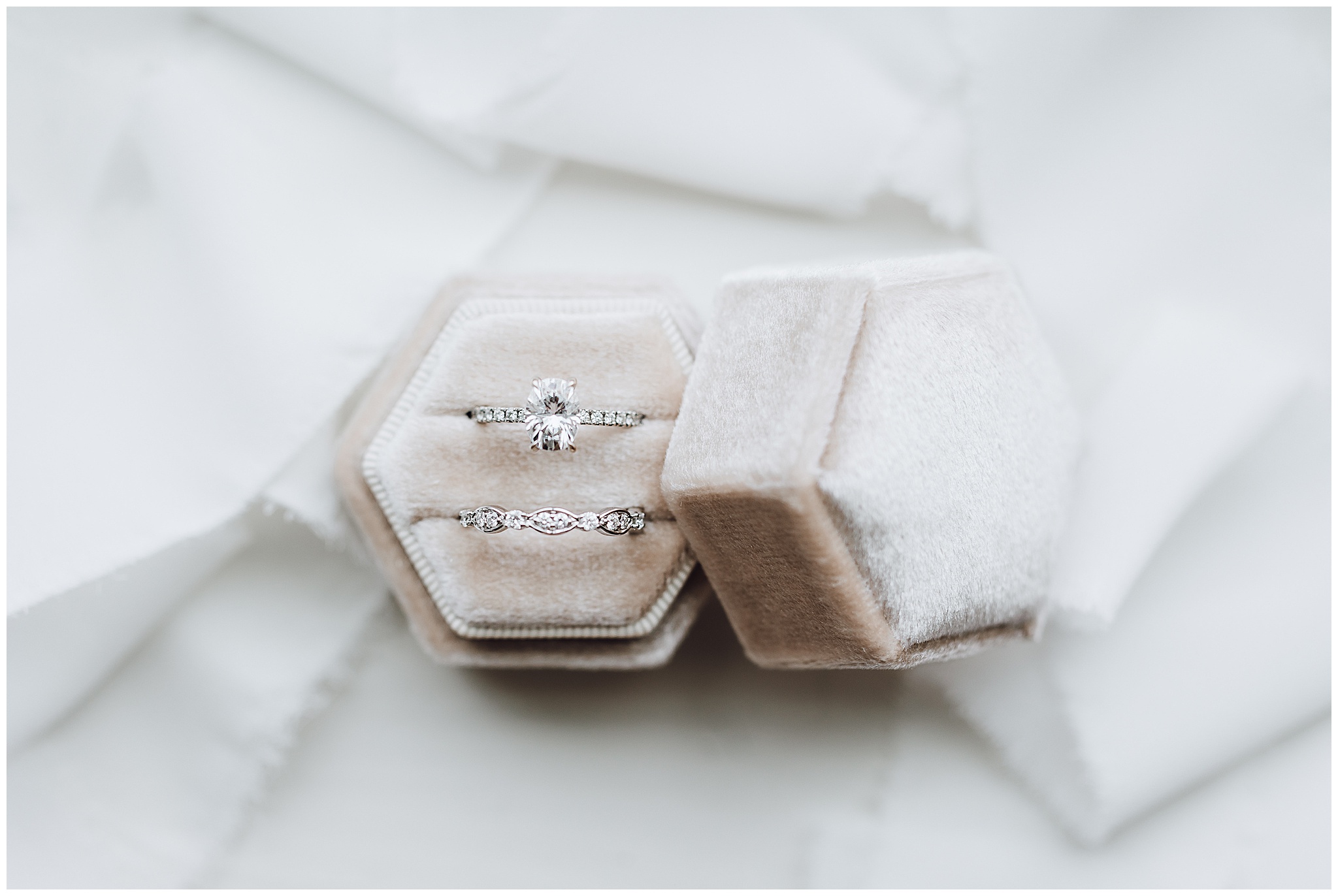 The bridal wedding rings sit in a tan ring box on a bed of white fabric