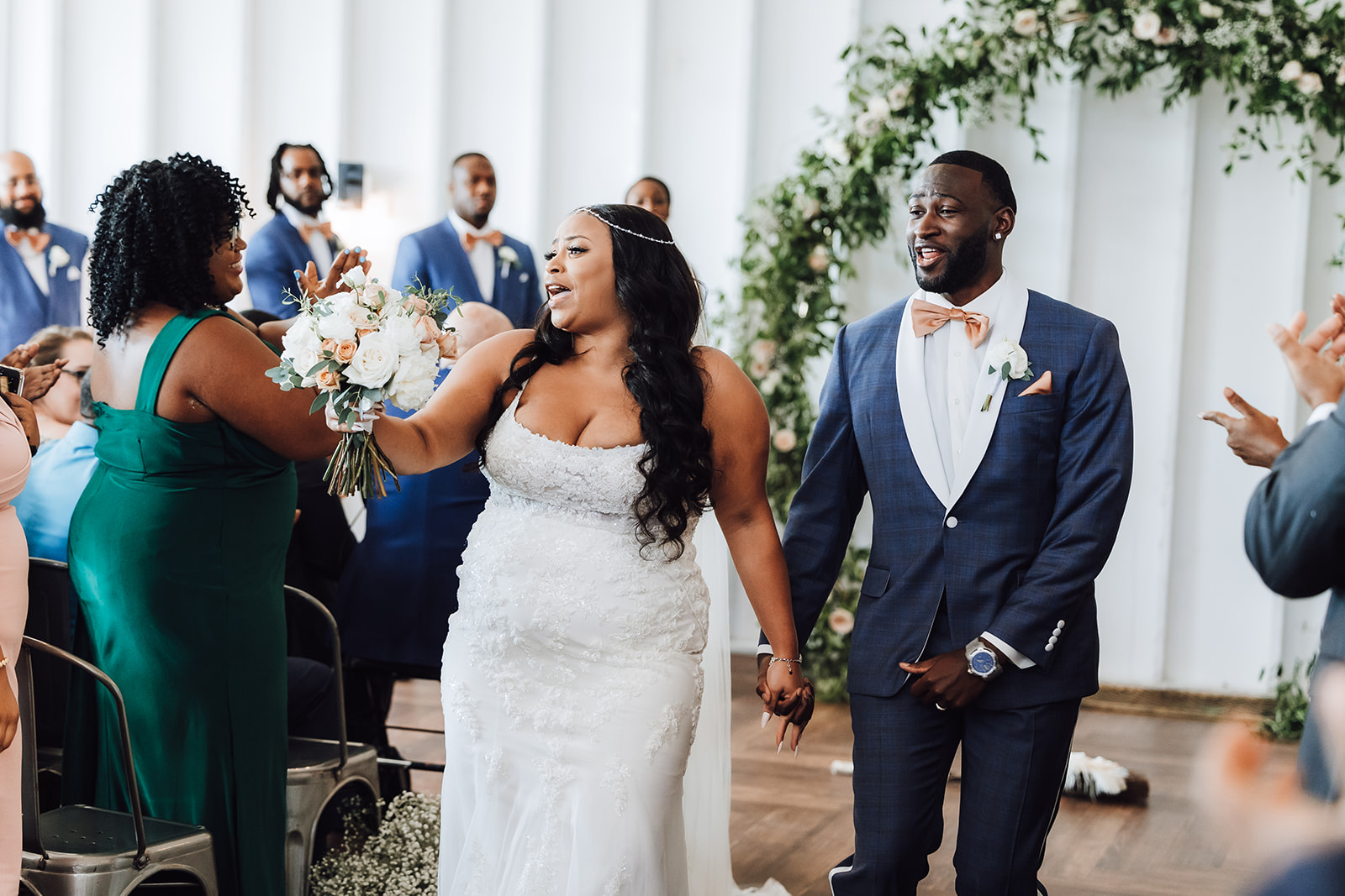 A bride and groom exit their wedding ceremony while their guests clap and cheer