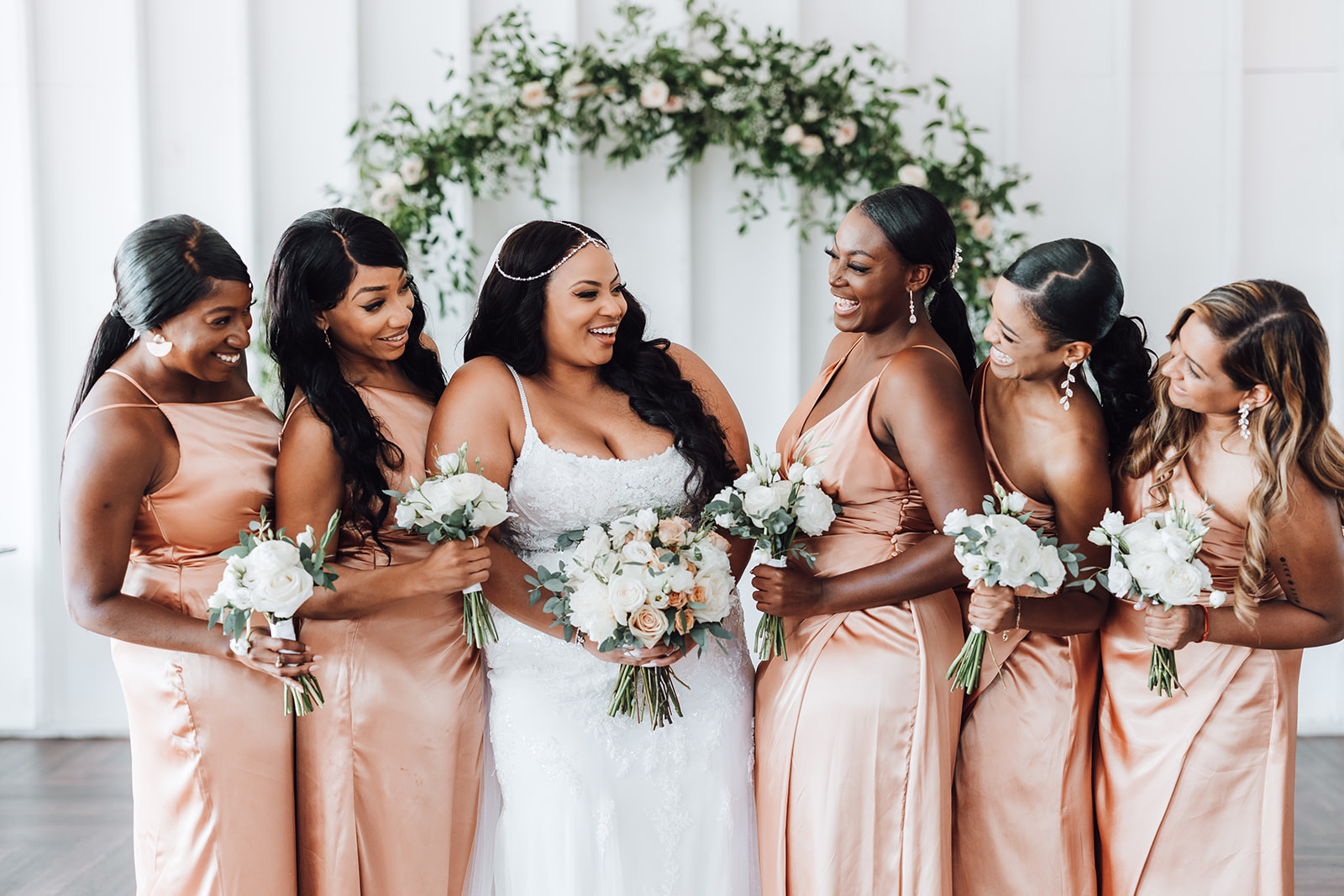 A bride and her wedding party laugh while holding their flowers