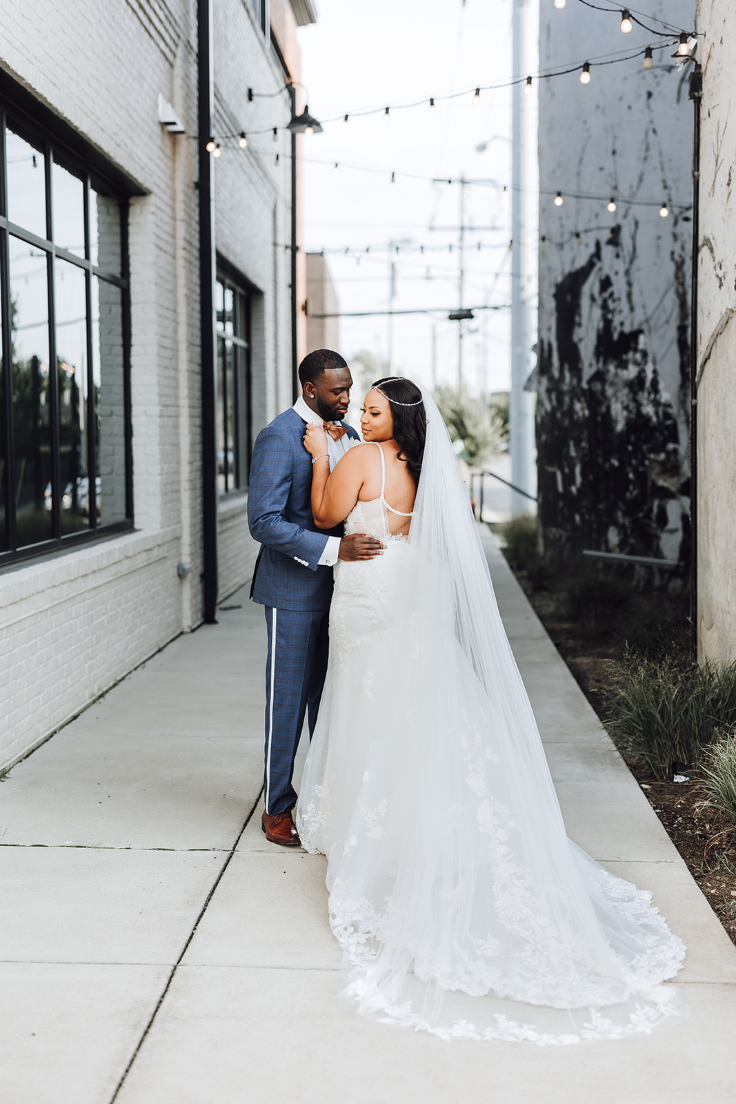 Newlyweds stand together in an alley surrounded by market lights 14Tenn Wedding