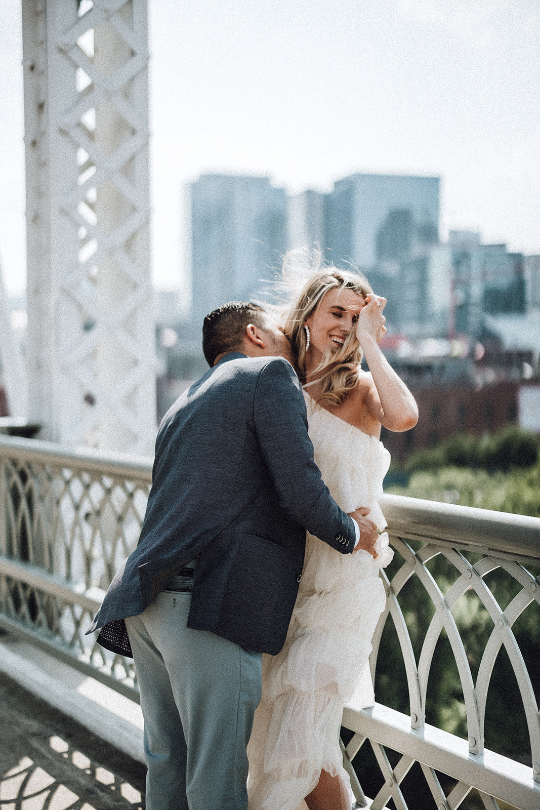 A groom kisses his bride's neck while standing on a bridge