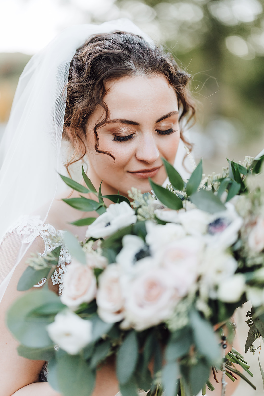 A bride looks down into her large bouquet in a long veil and lace dress