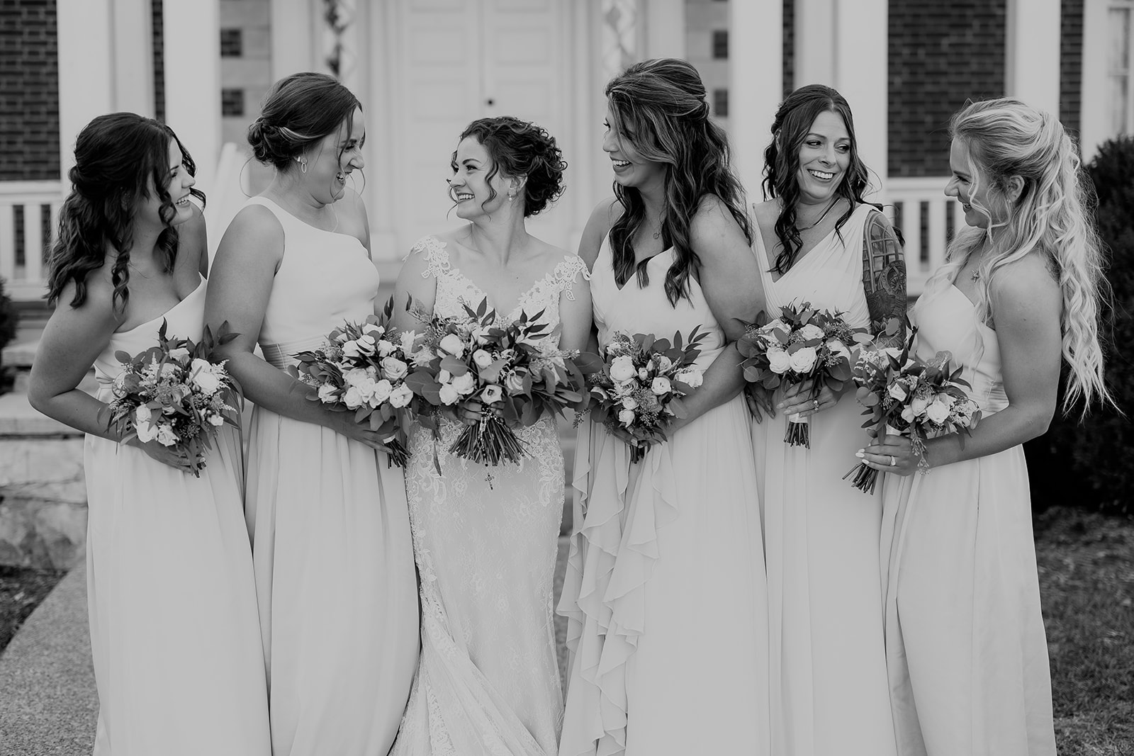 A bride stands with her bridesmaids outside a brick building holding their bouquets Ravenswood Mansion