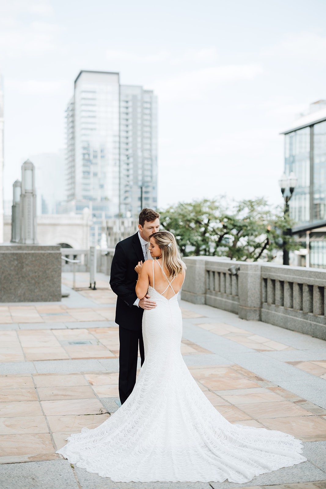 A groom kisses the head of his bride while standing on a stone patio
