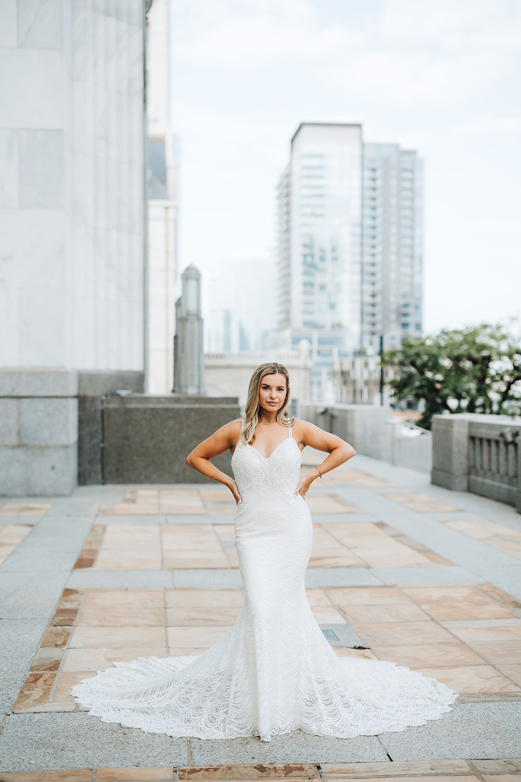 A bride in a long white lace dress stands on a stone patio with hands on her hips Union Station Wedding Nashville