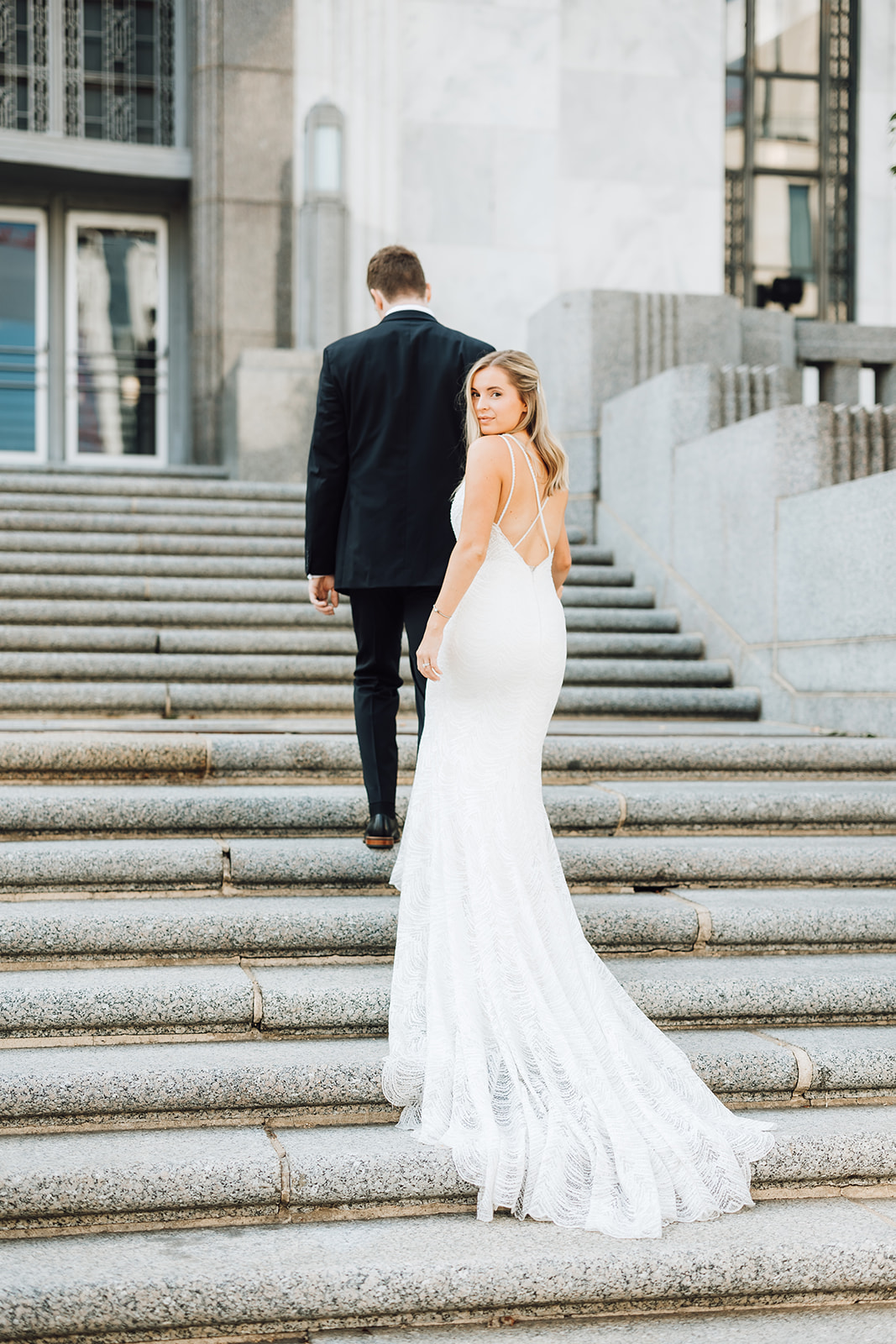 A bridge looks over her shoulder while walking up a set of stone stairs with her husband Union Station Wedding Nashville